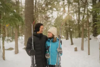 Couple souriant avec skis en forêt enneigée
