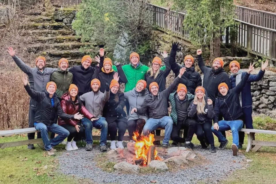 Group cheering around campfire wearing orange beanies