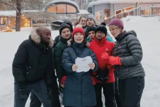 Group in winter coats reading paper outdoors