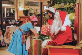 Père Noël offrant un cadeau devant sapin décoré