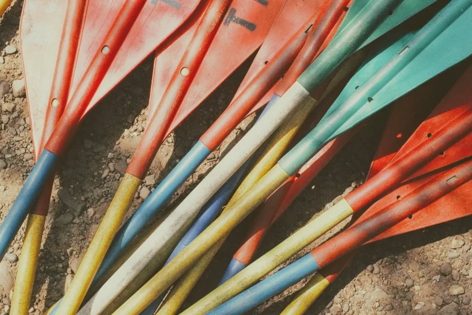 Colorful kayak paddles scattered on dirt ground