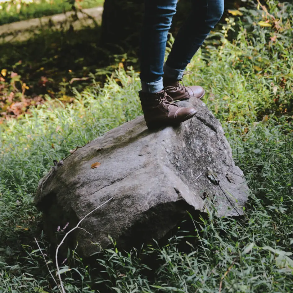 Person wearing boots standing on large rock outdoors
