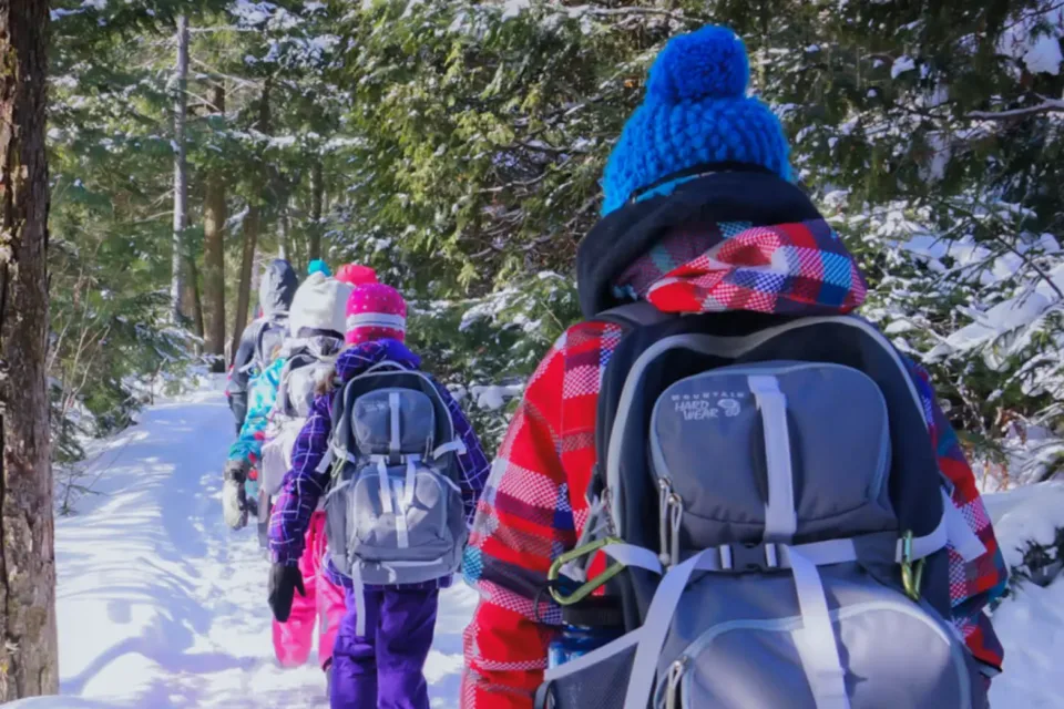 Children hiking through snowy forest with backpacks