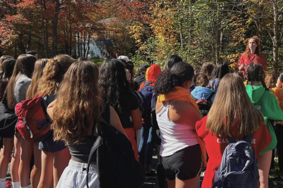 Students listening to counselor outdoors at fall camp