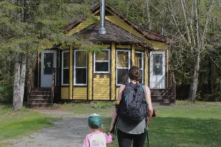 Femme et enfant devant chalet jaune en forêt