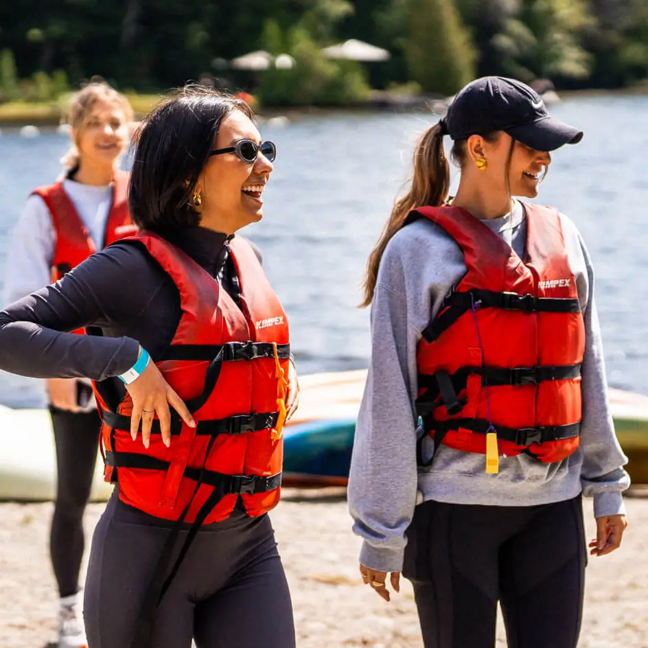 Three women wearing life jackets by lakeside