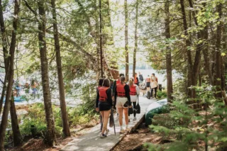 Group wearing life jackets walking toward lakeside canoes