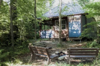 Blue cabin in woods with benches and fire pit