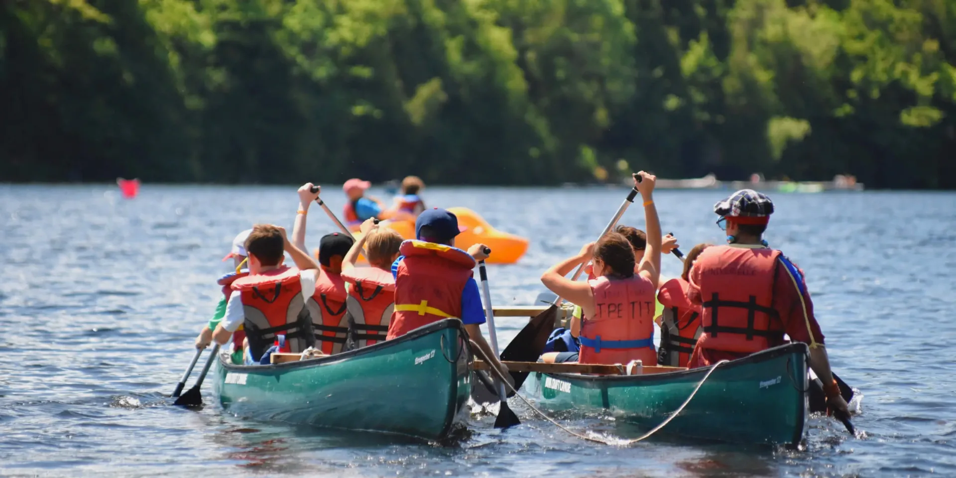 Children paddling canoes on a forest lake