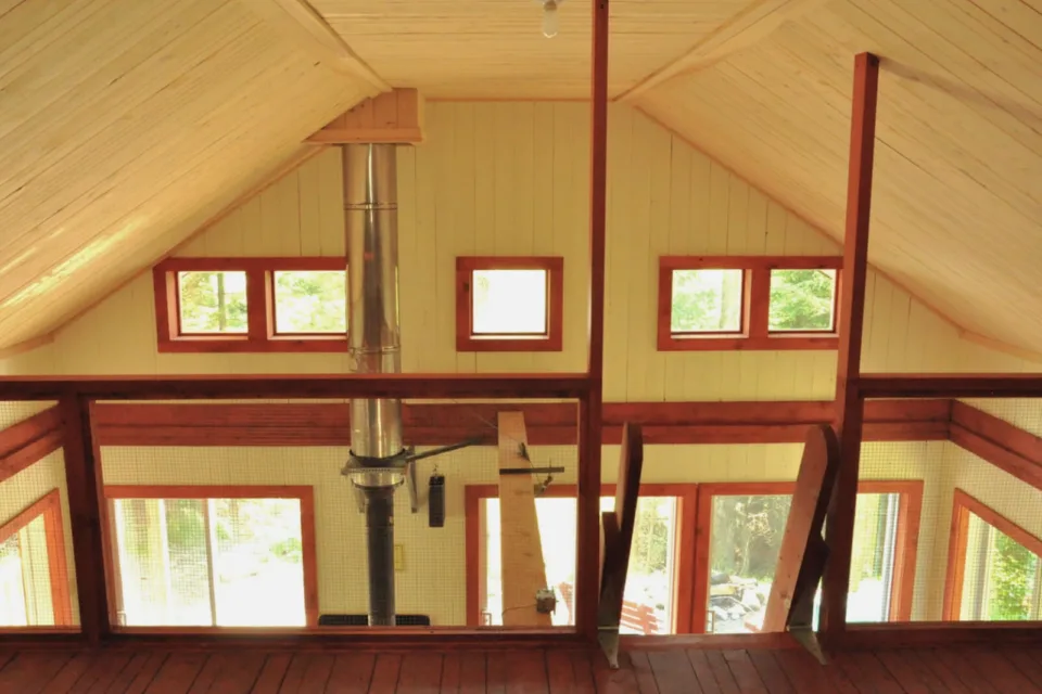 Wooden cabin loft with windows and metal stove pipe