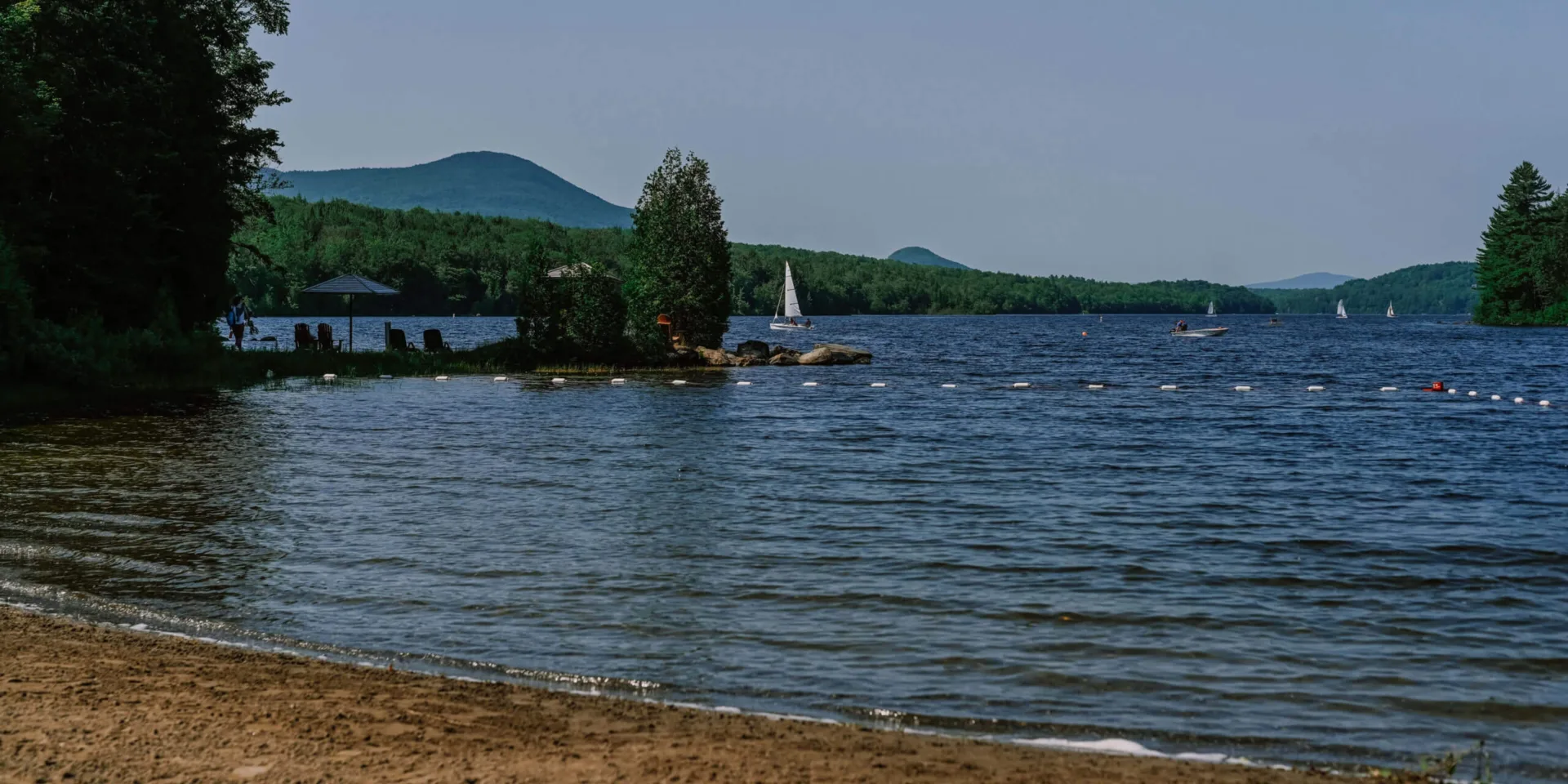Plage de lac avec voiliers et montagnes boisées