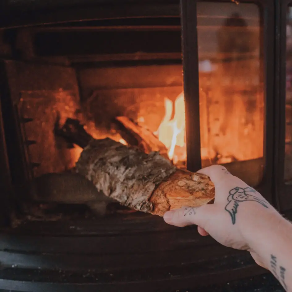 Hand placing log into wood-burning stove fire